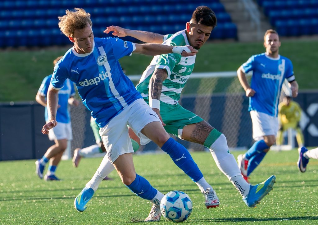 Annapolis Blues midfielder holds off a Santos Laguna defender while protecting the ball.